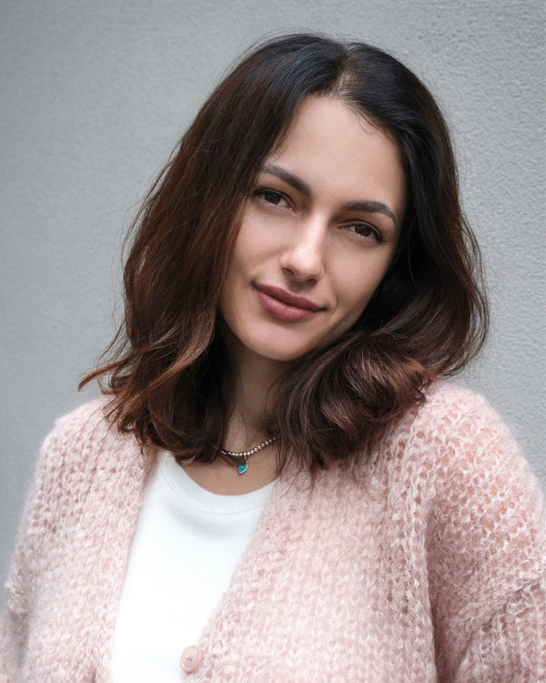 Woman with shoulder-length brown hair in a pink sweater on a gray backdrop, natural portrait NYC