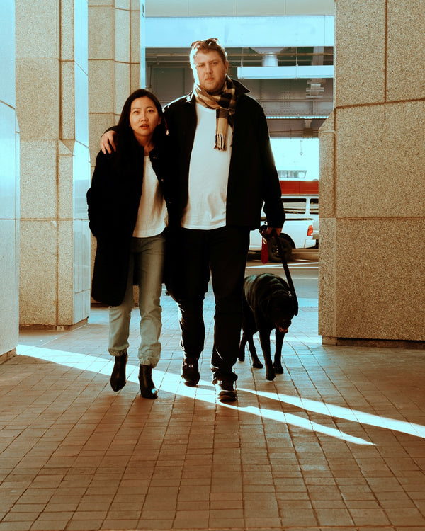 Couple walking their black dog through a sunlit New York arcade, candid NYC couples session