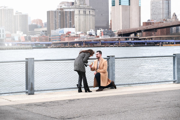 Proposal on one knee along the Brooklyn waterfront railing with the Manhattan skyline behind, NYC proposal photographer Lena Di