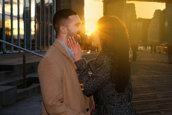 Couple embracing in backlit sunset glow on the Brooklyn waterfront, NYC engagement photography by Lena Di