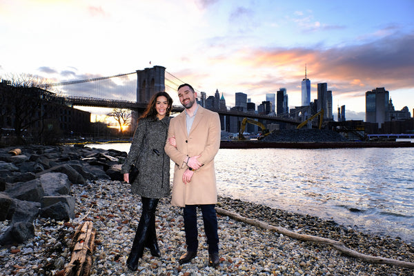 Engaged couple on a pebble beach at sunset with the Brooklyn Bridge and Manhattan skyline, NYC engagement photographer Lena Di
