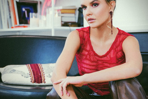 Model in a red top and drop earrings seated on a black sofa, NYC model portfolio by Lena Di