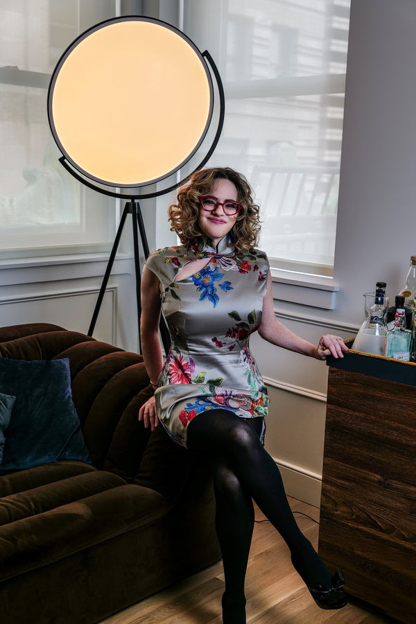 Woman in a floral dress seated by a studio light in a New York apartment, editorial portrait by Lena Di