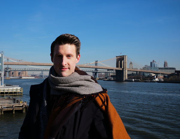 Smiling man in a scarf on the East River waterfront with the Brooklyn Bridge in the background, NYC portrait photographer Lena Di