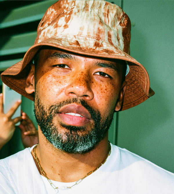 Color portrait of a man in a bucket hat against green foliage, editorial portrait photography in New York
