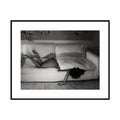 Hidden, black and white figure half-hidden under sofa cushions fine art photography print by Lena Di, shown framed with a white mat