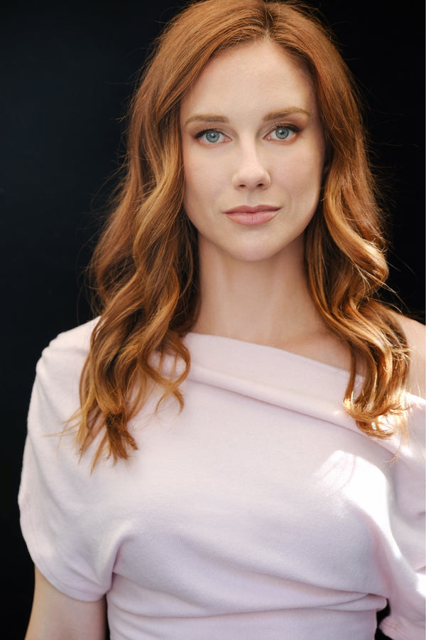 Red-haired woman in an off-shoulder blush top on a black backdrop, NYC portrait photography