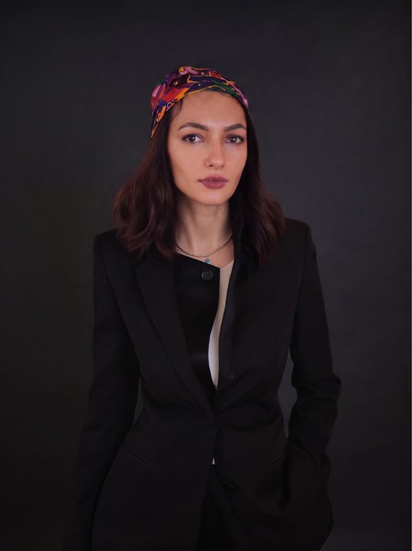 Woman with a red flower in her hair and a black blazer on a dark backdrop, editorial portrait