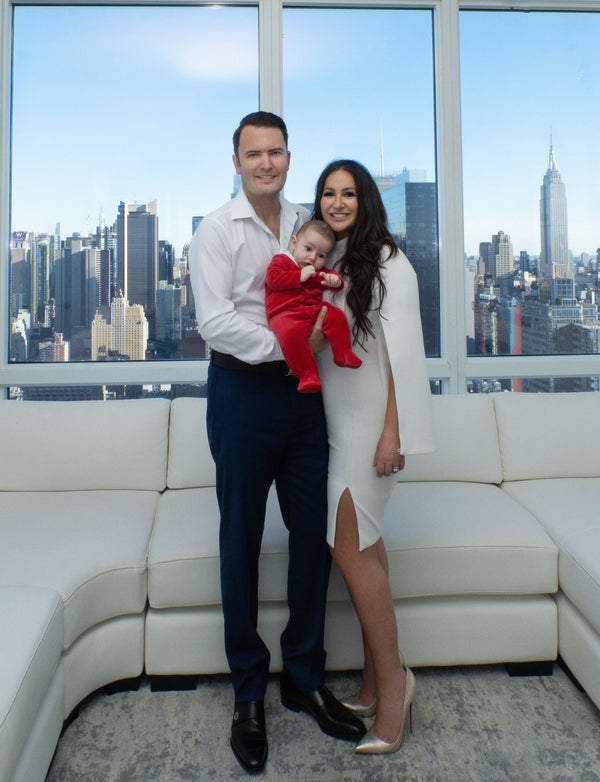 NYC family portrait: couple in white shirt and white dress holding their baby in red, full length in a bright Manhattan penthouse with skyline views