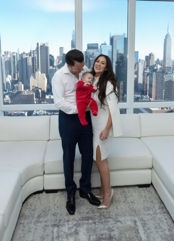 Candid NYC family photo: laughing mother with her baby in red and father looking down at him, Manhattan skyline behind, by Lena Di