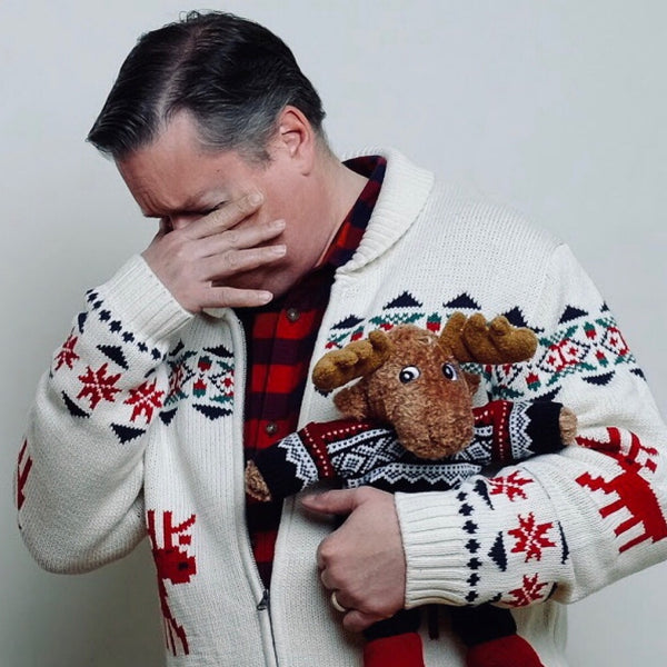 Holiday family photo of a father laughing behind his hand while holding a reindeer plush, NYC family photographer Lena Di