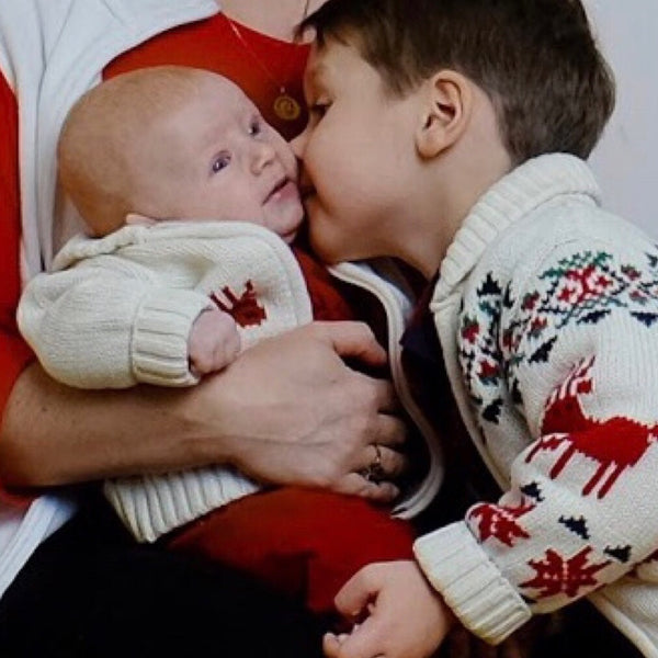 Holiday family photo of a big brother kissing his baby brother in matching Christmas sweaters, NYC family photographer Lena Di
