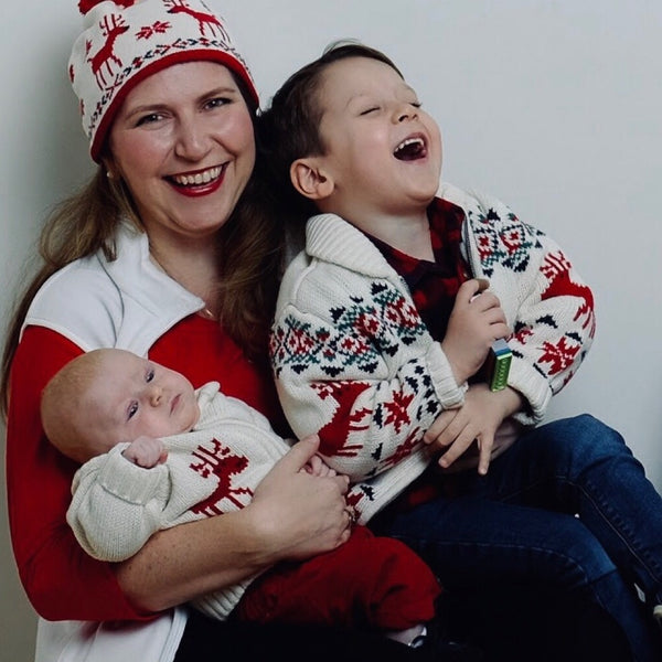 Holiday family photo of a smiling mother in a reindeer hat with her baby and laughing son, NYC family photographer Lena Di