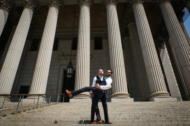 Two grooms celebrating on the 60 Centre St courthouse steps after their City Hall wedding, NYC wedding photography by Lena Di