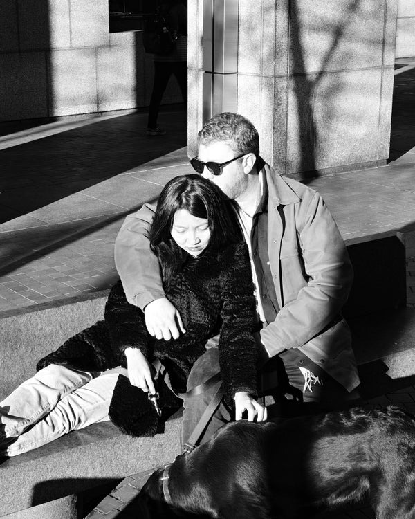 Black and white photo of a couple relaxing in the sun with their dog on a Manhattan plaza, NYC couples photographer Lena Di