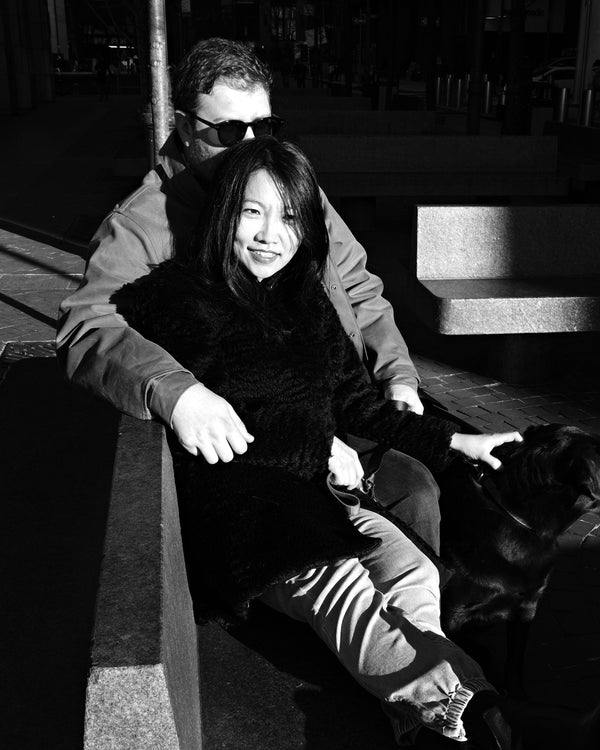 Couple laughing together on a sunlit bench with their dog, black and white NYC couples session