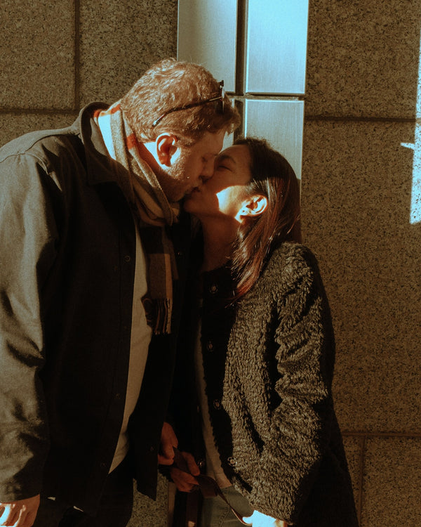 Couple kissing in warm winter light beside a building, NYC couples photography by Lena Di