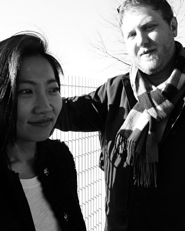 Smiling couple by a riverside fence in black and white, NYC couples photography by Lena Di