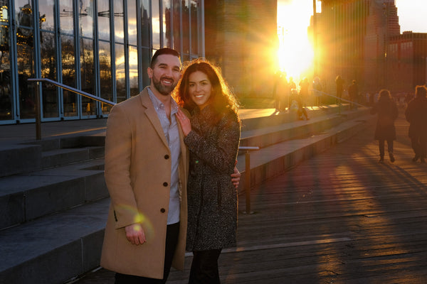 Engaged couple standing in golden sunset light on a Brooklyn boardwalk, NYC engagement photographer Lena Di