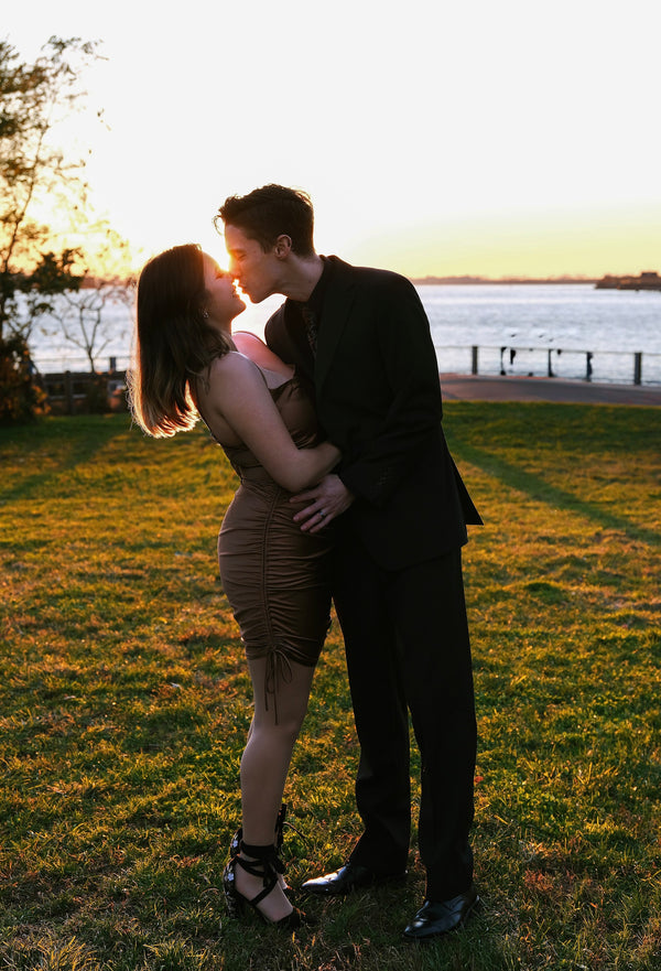 Couple kissing at sunset on the grass by the water, backlit golden-hour NYC couples photography by Lena Di