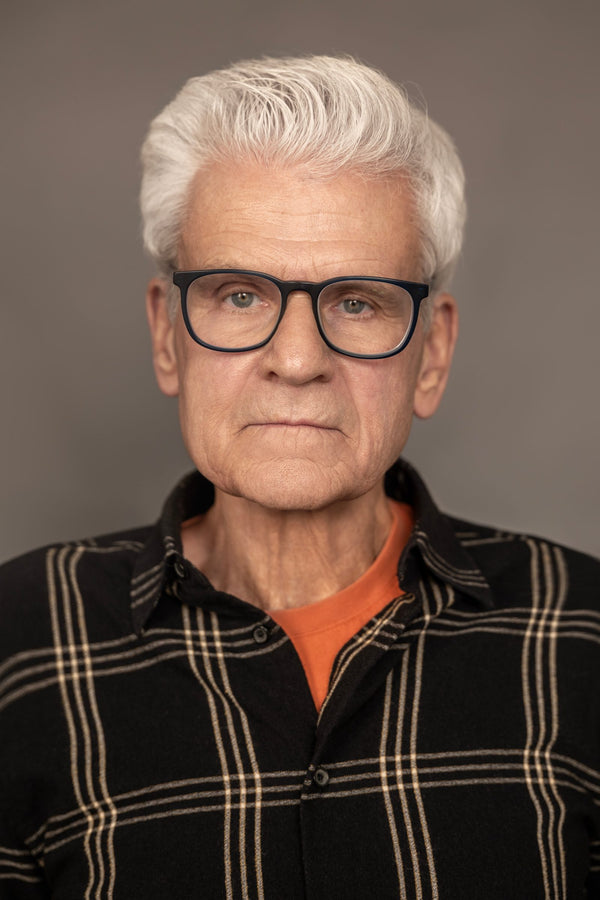 Professional headshot in NYC – silver-haired man in glasses on a warm gray studio backdrop