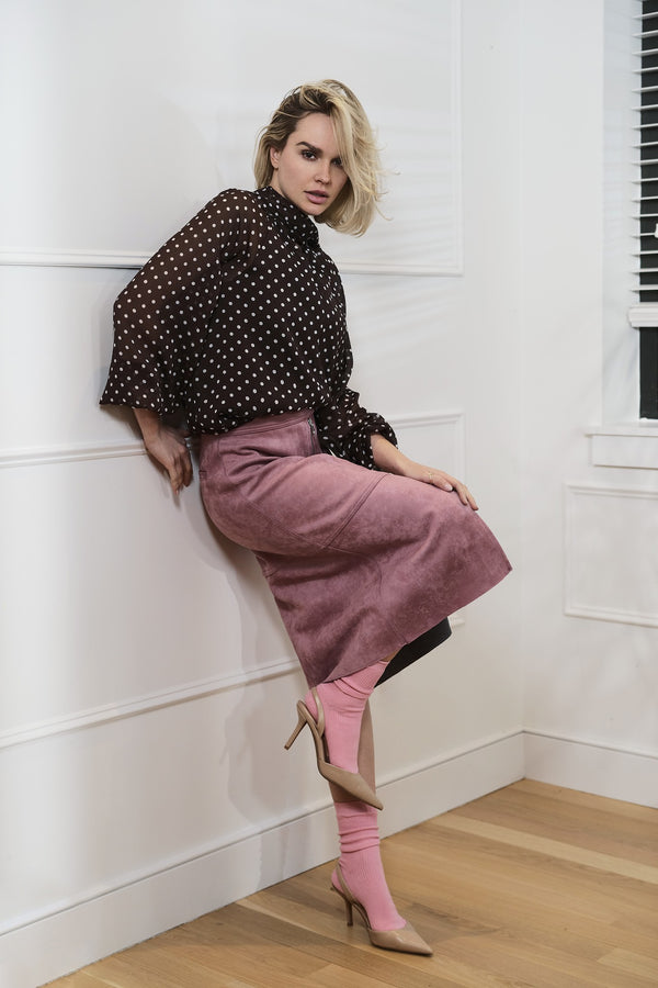 Model in a polka-dot blouse and pink skirt leaning on a wall, NYC fashion portfolio by Lena Di