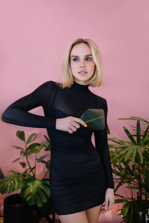 Model in a black turtleneck dress against a pink wall with plants, NYC model portfolio by Lena Di