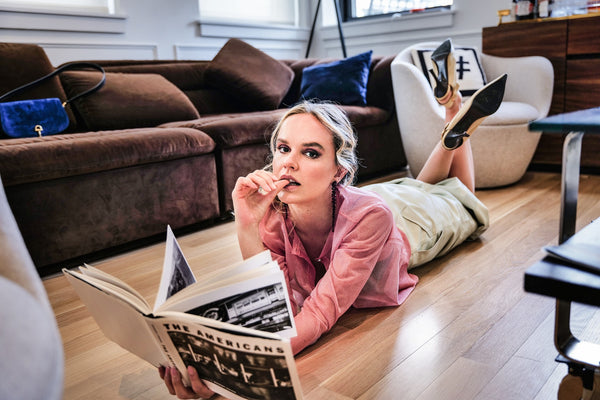 Model in a pink sweater lying on a wood floor reading a magazine, editorial model portfolio in NYC by Lena Di