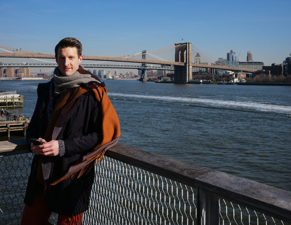 Full-length portrait of a man in a winter coat by the East River with the Brooklyn Bridge, NYC portrait photographer Lena Di
