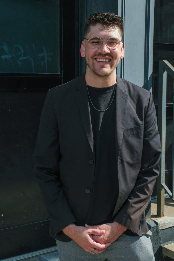 Smiling man in a black blazer standing in a sunlit doorway, environmental portrait by NYC portrait photographer Lena Di