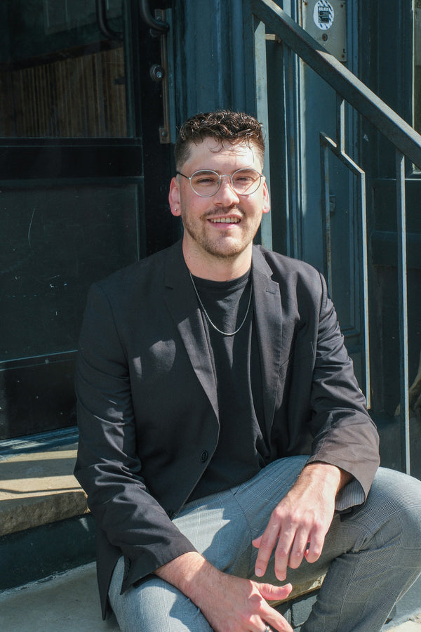 Smiling man in glasses and a blazer seated on sunlit steps, NYC portrait photographer Lena Di