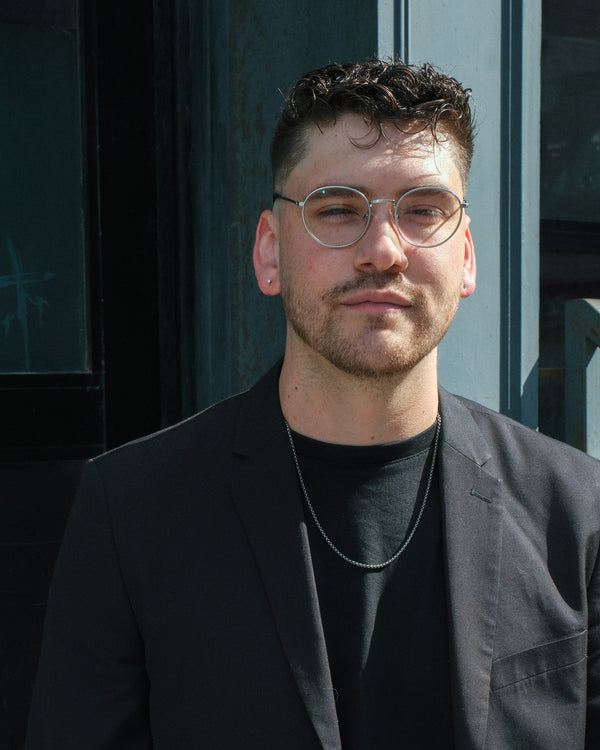 Close portrait of a man in glasses and a black blazer in warm window light, NYC portrait photographer Lena Di