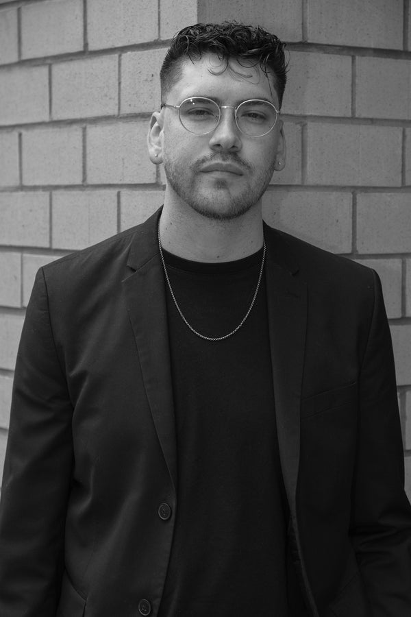 Black and white portrait of a man in glasses and a blazer against a brick wall, NYC portrait photographer Lena Di
