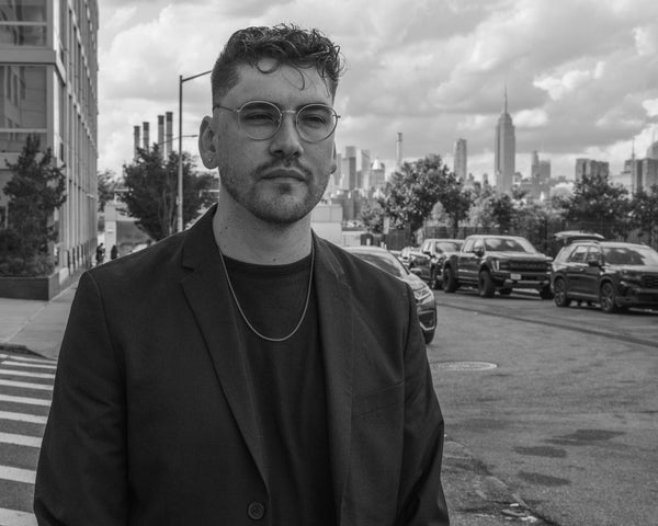Black and white street portrait of a man in a blazer with the Manhattan skyline behind, NYC portrait photographer Lena Di
